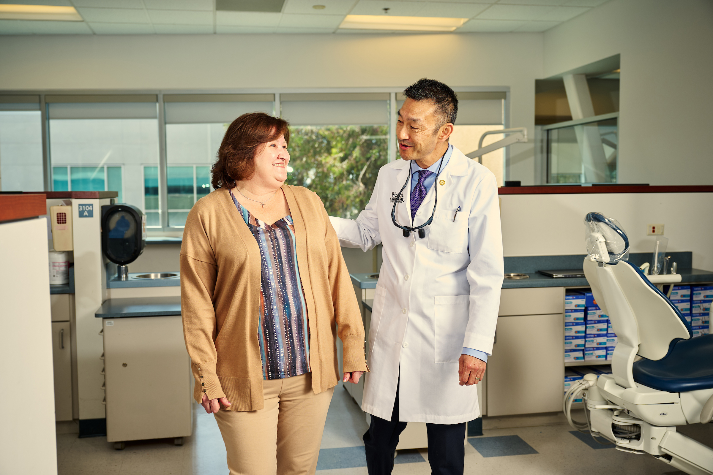 A female patient walking beside a male dentist in a treatment room inside the dental center